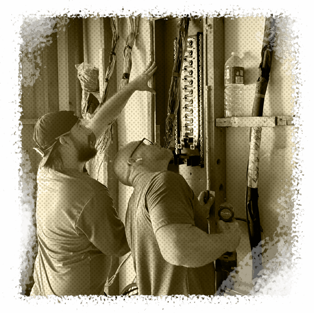 Two electricians inspecting a circuit breaker panel, discussing electrical wiring safety and compliance in a residential setting.
