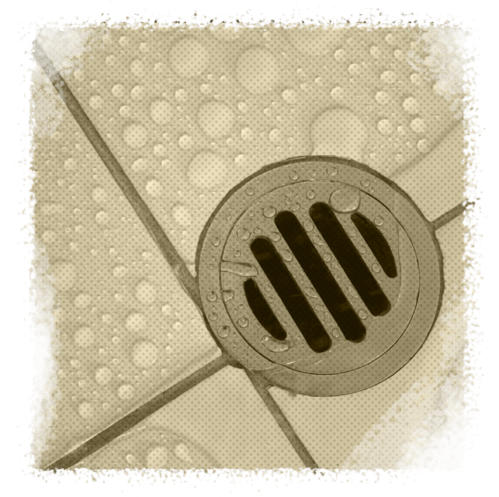 Drain cover in a tiled floor with water droplets, representing sewer service issues in Houston, TX.