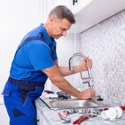 Plumber installing a kitchen faucet with tools on a countertop, highlighting plumbing installation services.